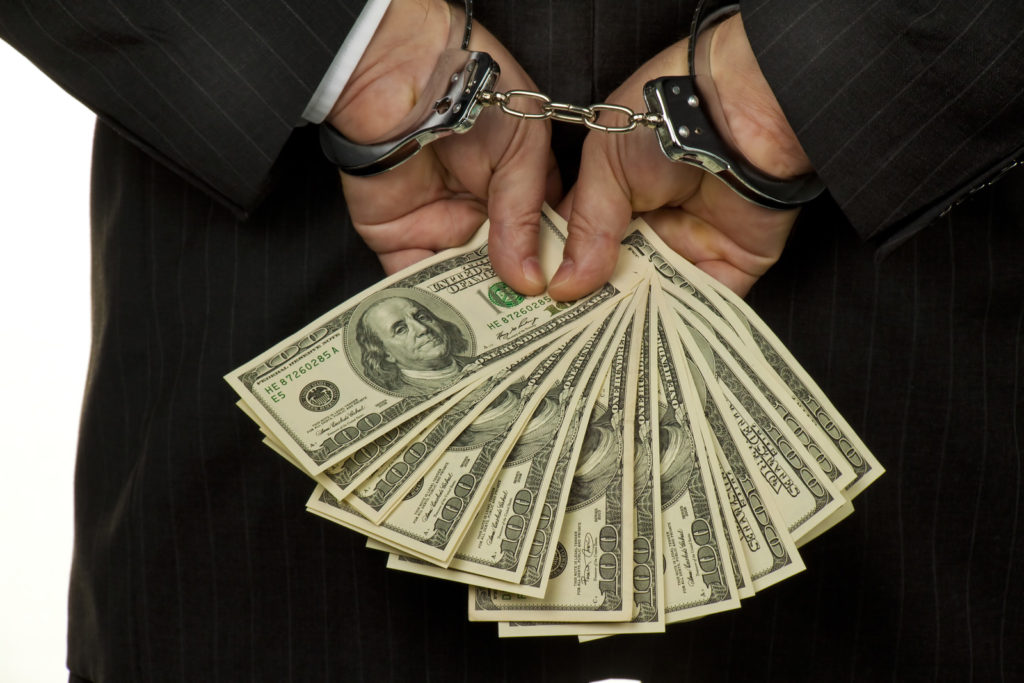 Businessman, handcuffed hands behind his back, holding $100 bills.